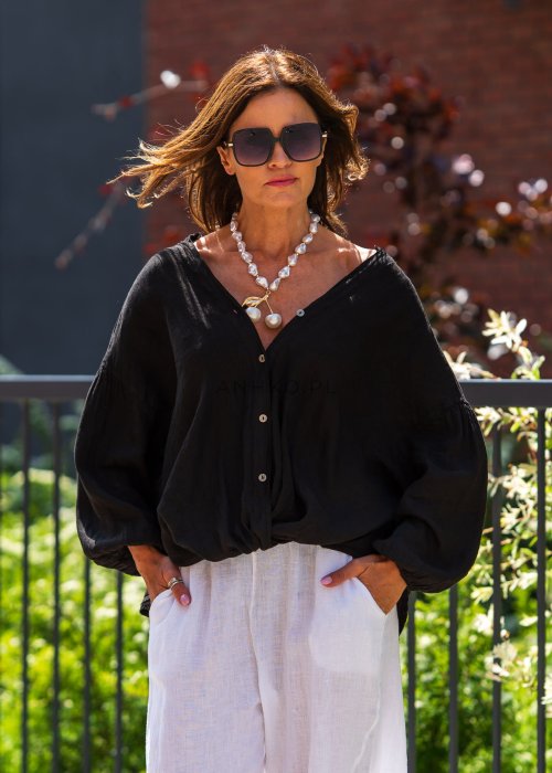 Czarna lniana koszula damska oversize z dekoltem V i guzikami, zestawiona z jasnymi spodniami w eleganckiej, miejskiej stylizacji.