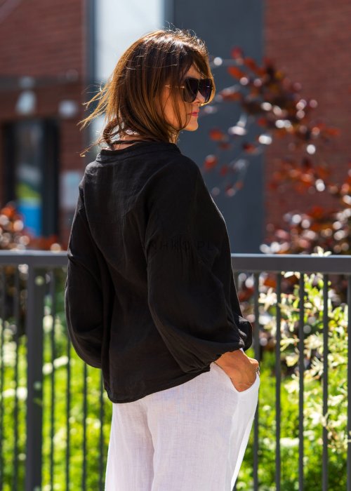 Czarna lniana koszula damska oversize z dekoltem V i guzikami, zestawiona z jasnymi spodniami w eleganckiej, miejskiej stylizacji.