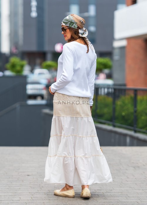 Biała prążkowana bluzka damska z długim rękawem i dekoltem zapinanym na guziki, zestawiona z jasną spódnicą w miejskiej stylizacji.