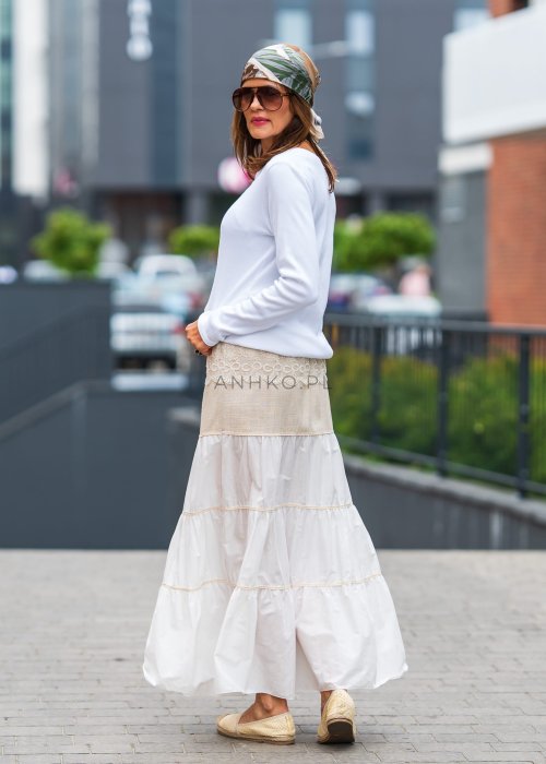 Biała prążkowana bluzka damska z długim rękawem i dekoltem zapinanym na guziki, zestawiona z jasną spódnicą w miejskiej stylizacji.