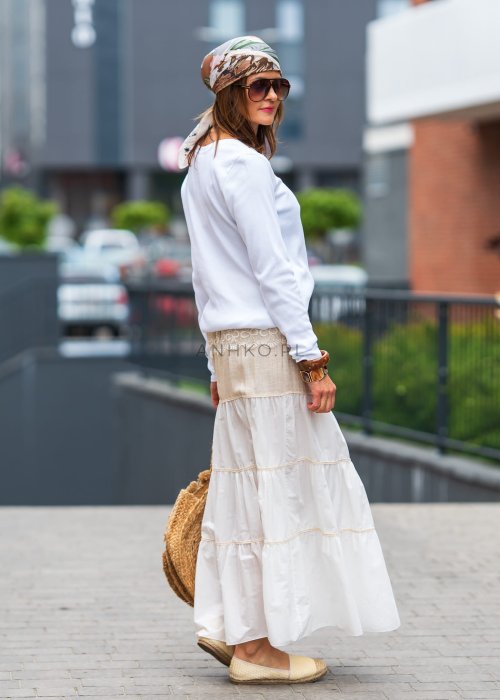 Biała prążkowana bluzka damska z długim rękawem i dekoltem zapinanym na guziki, zestawiona z jasną spódnicą w miejskiej stylizacji.