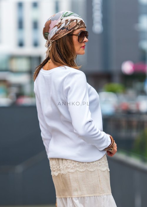 Biała prążkowana bluzka damska z długim rękawem i dekoltem zapinanym na guziki, zestawiona z jasną spódnicą w miejskiej stylizacji.
