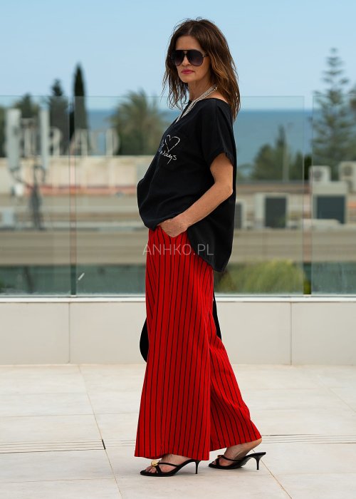 Czerwone spodnie damskie w czarne pionowe paski o szerokim kroju, zestawione z czarną bluzą i botkami na obcasie w nowoczesnej stylizacji.