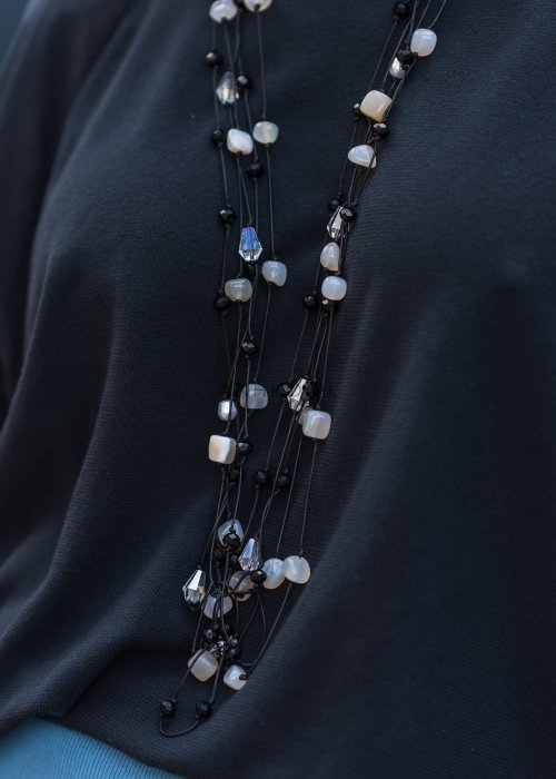 Długi naszyjnik damski na cienkich sznurkach z czarnymi i perłowymi koralikami oraz drobnymi kryształkami o nieregularnym kształcie.