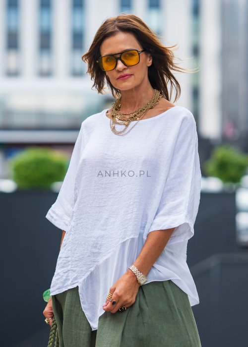 Biała bluzka lniana oversize z asymetrycznym dołem i lekką transparentną wstawką, zestawiona z zielonymi spodniami w stylizacji miejskiej.