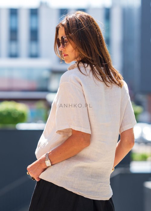 Beżowa bluzka lniana z krótkim rękawem i czarnym, artystycznym haftem na przodzie. Stylizacja z czarną spódnicą maxi i minimalistyczną biżuterią.