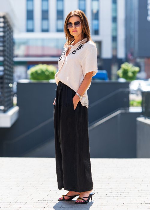 Beżowa bluzka lniana z krótkim rękawem i czarnym, artystycznym haftem na przodzie. Stylizacja z czarną spódnicą maxi i minimalistyczną biżuterią.