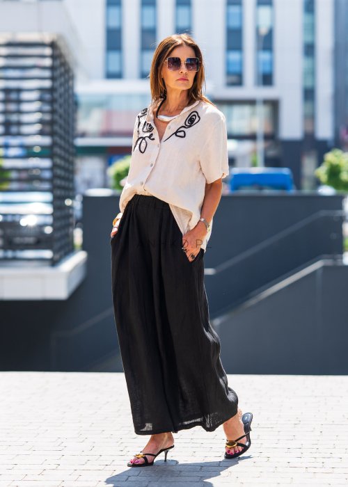 Beżowa bluzka lniana z krótkim rękawem i czarnym, artystycznym haftem na przodzie. Stylizacja z czarną spódnicą maxi i minimalistyczną biżuterią.