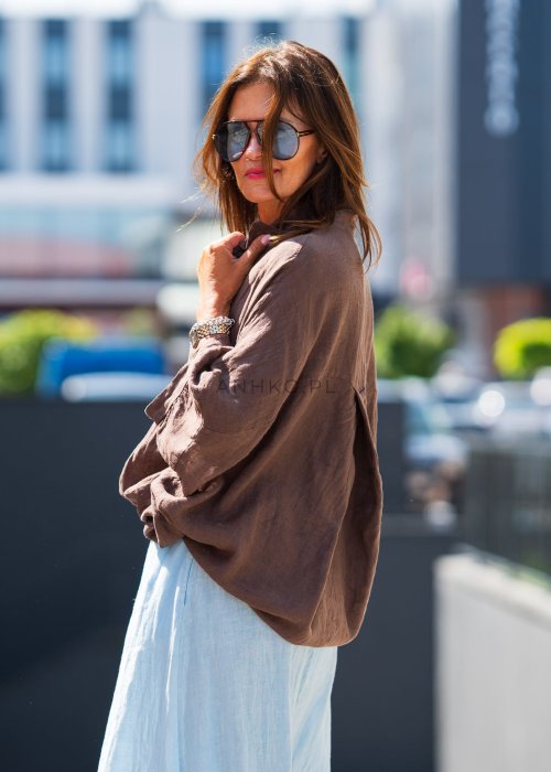 Brązowa koszula lniana damska o luźnym kroju z kołnierzykiem i kieszonką na piersi, zestawiona z jasną, lnianą spódnicą i dodatkami w naturalnym stylu.