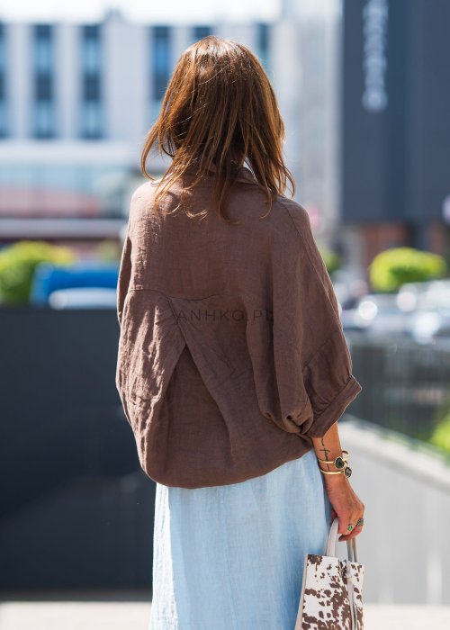 Brązowa koszula lniana damska o luźnym kroju z kołnierzykiem i kieszonką na piersi, zestawiona z jasną, lnianą spódnicą i dodatkami w naturalnym stylu.