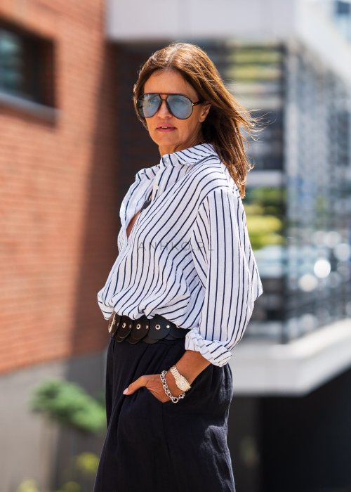 Lniana koszula damska biała w granatowe paski, luźny fason z kołnierzykiem i guzikami, stylizacja z czarną spódnicą i paskiem.