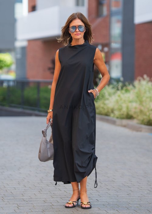 Czarna sukienka maxi bez rękawów ze stójką i regulowanym dołem na troczki. Modelka prezentuje minimalistyczną miejską stylizację z sandałami i torebką.