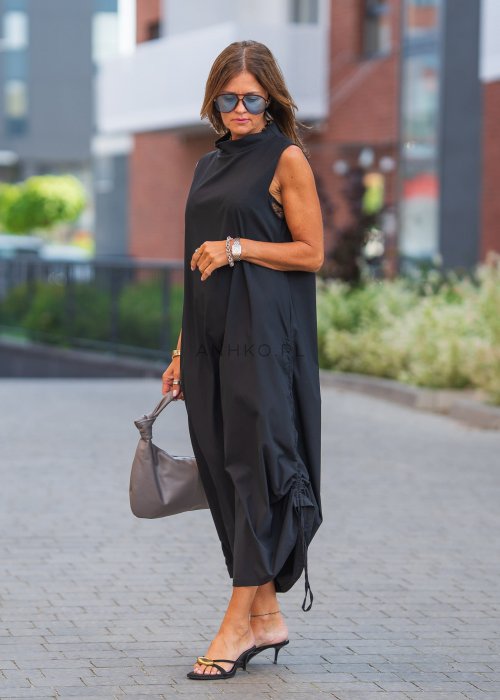 Czarna sukienka maxi bez rękawów ze stójką i regulowanym dołem na troczki. Modelka prezentuje minimalistyczną miejską stylizację z sandałami i torebką.