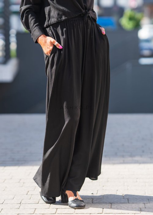 Czarny komplet z lekkiej, przewiewnej tkaniny – bluza z kapturem i wiązaniem w talii oraz długa, swobodna spódnica. Elegancja i wygoda w jednym.