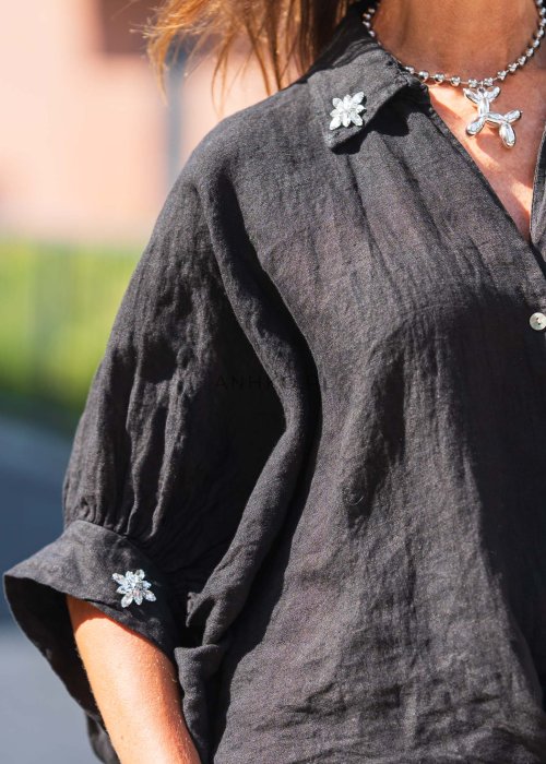 Czarna lniana koszula oversize z kołnierzykiem i wiązaniem z przodu, ozdobiona aplikacjami, zestawiona z jasnymi szortami w paski