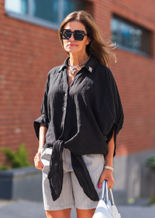 Czarna lniana koszula oversize z kołnierzykiem i wiązaniem z przodu, ozdobiona aplikacjami, zestawiona z jasnymi szortami w paski