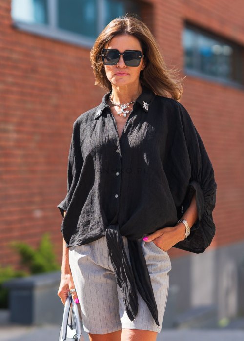 Czarna lniana koszula oversize z kołnierzykiem i wiązaniem z przodu, ozdobiona aplikacjami, zestawiona z jasnymi szortami w paski