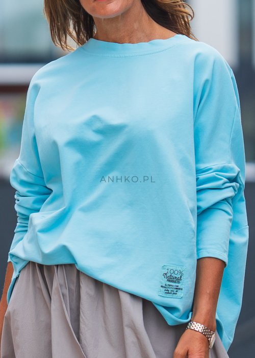 Bluza damska oversize w kolorze baby blue z długim rękawem i naszywką na froncie. Luźny fason w stylizacji z szeroką spódnicą i dodatkami w miejskim stylu.