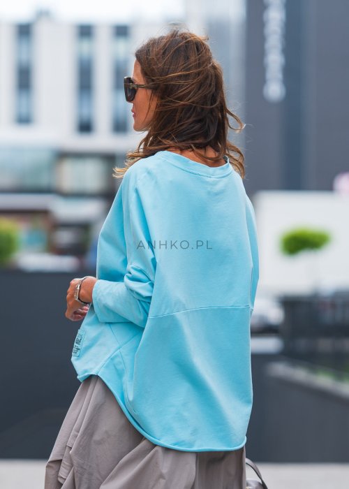 Bluza damska oversize w kolorze baby blue z długim rękawem i naszywką na froncie. Luźny fason w stylizacji z szeroką spódnicą i dodatkami w miejskim stylu.