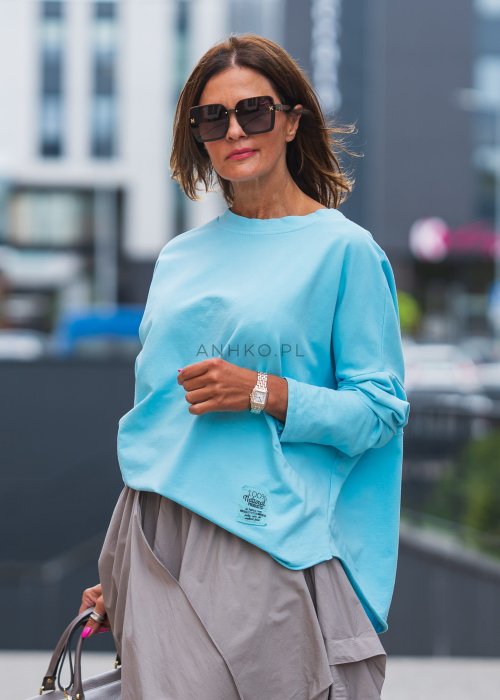 Bluza damska oversize w kolorze baby blue z długim rękawem i naszywką na froncie. Luźny fason w stylizacji z szeroką spódnicą i dodatkami w miejskim stylu.
