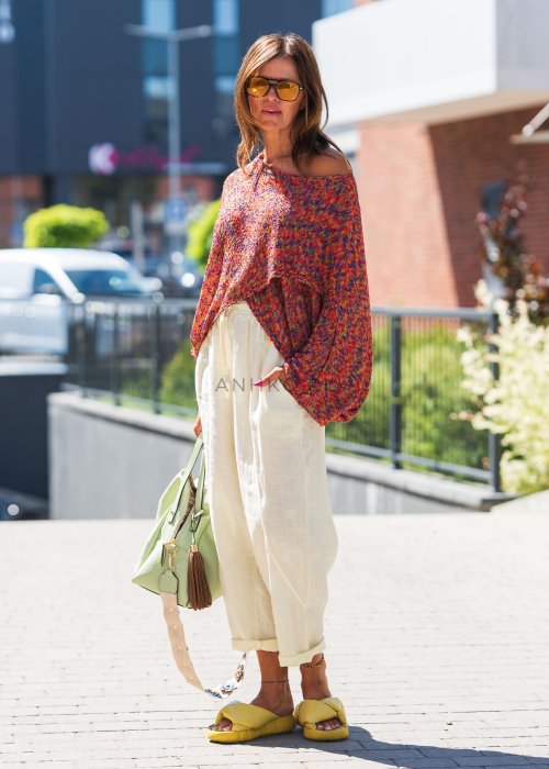 Kolorowy sweter oversize multicolor z teksturowanej dzianiny i szerokimi rękawami, zestawiony z jasnymi lnianymi spodniami w nowoczesnej miejskiej stylizacji.