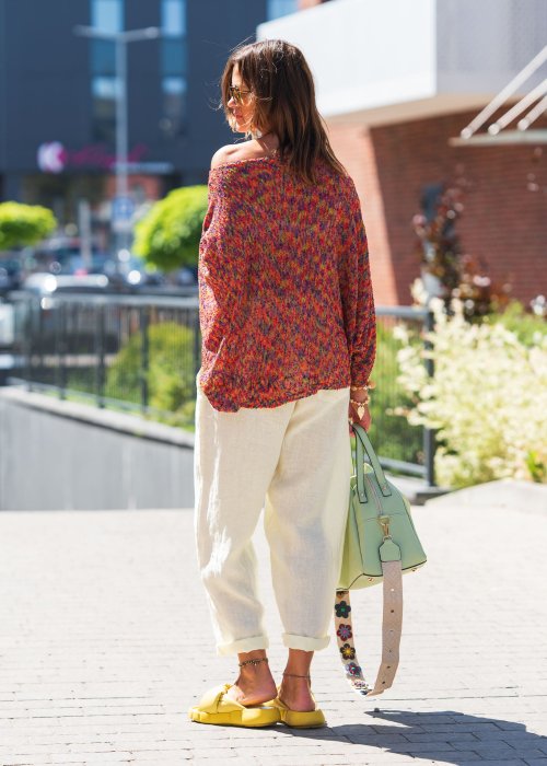 Kolorowy sweter oversize multicolor z teksturowanej dzianiny i szerokimi rękawami, zestawiony z jasnymi lnianymi spodniami w nowoczesnej miejskiej stylizacji.