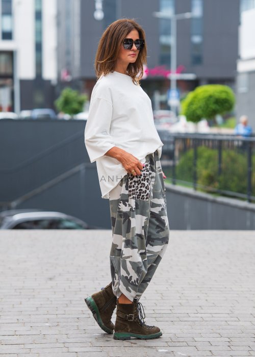 Biała bluzka oversize damska z szerokim dekoltem i haftowanym detalem na rękawie, zestawiona ze spodniami moro w casualowej stylizacji miejskiej.