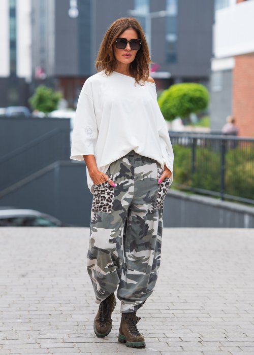 Biała bluzka oversize damska z szerokim dekoltem i haftowanym detalem na rękawie, zestawiona ze spodniami moro w casualowej stylizacji miejskiej.