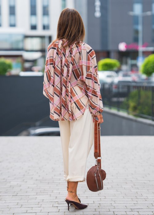 Wzorzysta bluzka w różowo-brązową kratę, kremowe spodnie i brązowy pasek, do tego duże okulary i delikatny naszyjnik.