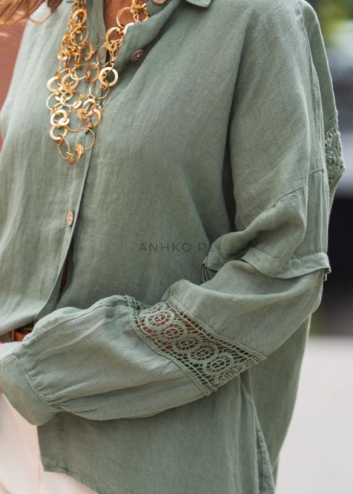 Długa, oliwkowa koszula z koronkowymi wstawkami na rękawach, białe spodnie i złoty naszyjnik.