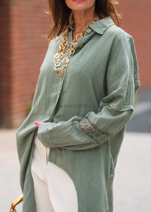 Długa, oliwkowa koszula z koronkowymi wstawkami na rękawach, białe spodnie i złoty naszyjnik.