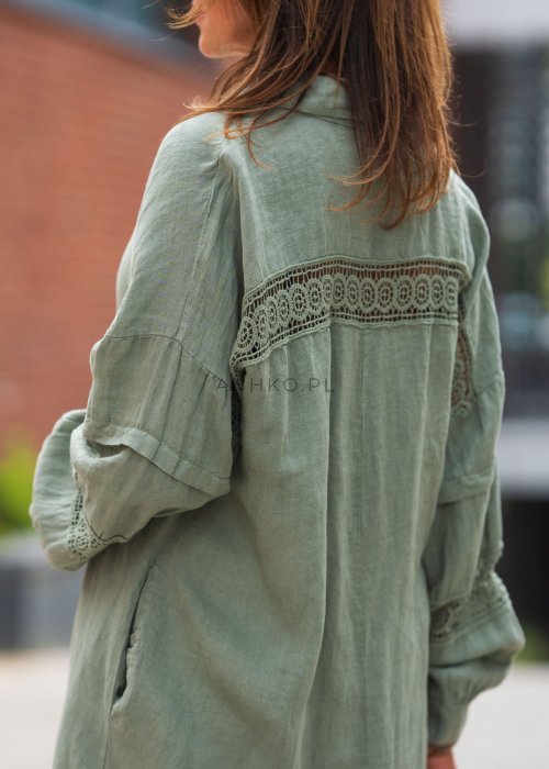 Długa, oliwkowa koszula z koronkowymi wstawkami na rękawach, białe spodnie i złoty naszyjnik.