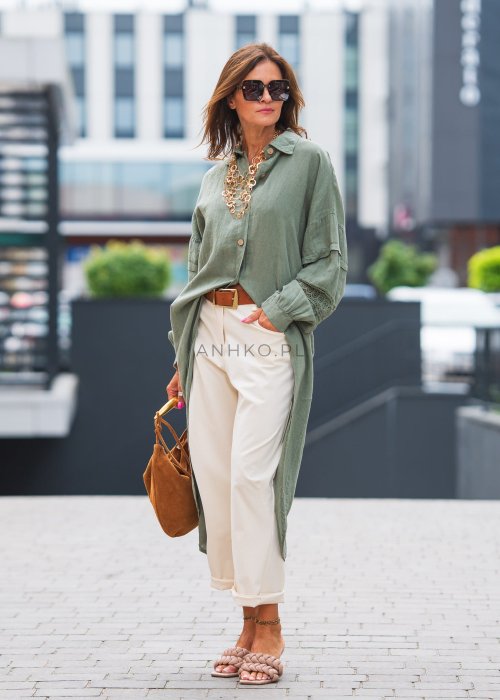 Długa, oliwkowa koszula z koronkowymi wstawkami na rękawach, białe spodnie i złoty naszyjnik.