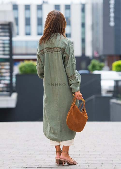 Długa, oliwkowa koszula z koronkowymi wstawkami na rękawach, białe spodnie i złoty naszyjnik.