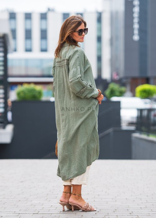 Długa, oliwkowa koszula z koronkowymi wstawkami na rękawach, białe spodnie i złoty naszyjnik.