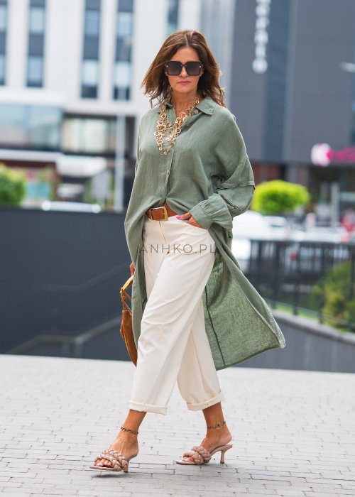Długa, oliwkowa koszula z koronkowymi wstawkami na rękawach, białe spodnie i złoty naszyjnik.