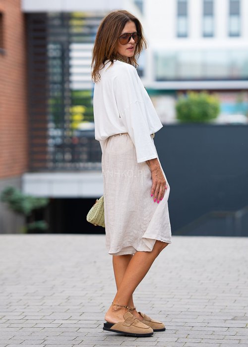 Biała bluzka z długim rękawem, o luźnym kroju, z dekoltem w serek ozdobionym dużym kwiatem z tkaniny po lewej stronie.