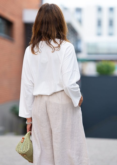 Biała bluzka z długim rękawem, o luźnym kroju, z dekoltem w serek ozdobionym dużym kwiatem z tkaniny po lewej stronie.