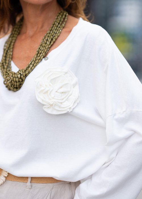 Biała bluzka z długim rękawem, o luźnym kroju, z dekoltem w serek ozdobionym dużym kwiatem z tkaniny po lewej stronie.