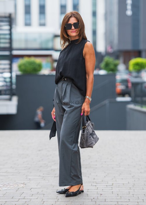 Szare, eleganckie spodnie z wysokim stanem i zakładkami z przodu, uzupełnione czarnym paskiem, zestawione z czarnymi, lakierowanymi mokasynami.