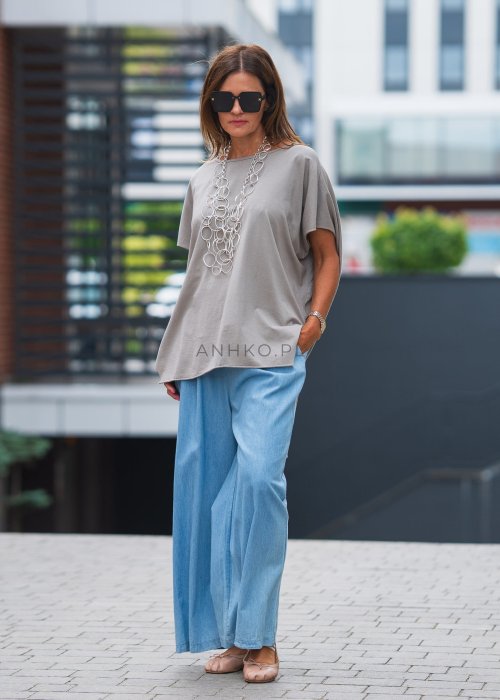 Bluzka oversize taupe z asymetrycznym dołem i wydłużonym tyłem, zestawiona z jasnymi jeansami. Luźny fason tworzy nowoczesną, minimalistyczną stylizację.