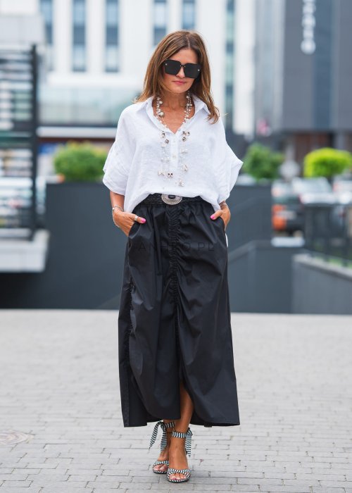 Biała, luźna koszula z kołnierzykiem, czarne spodnie z ozdobnym paskiem i długi naszyjnik z perełkami.