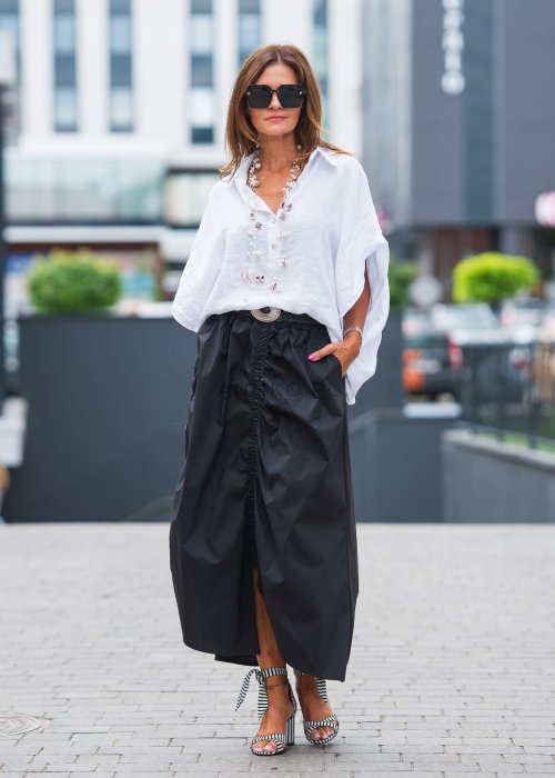 Biała, luźna koszula z kołnierzykiem, czarne spodnie z ozdobnym paskiem i długi naszyjnik z perełkami.