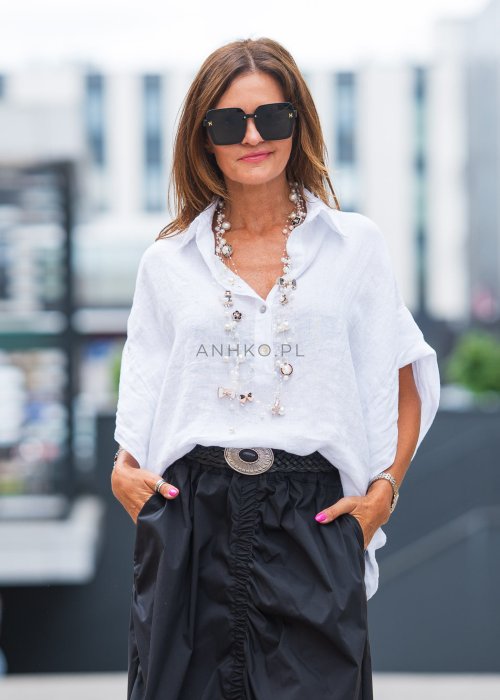 Biała, luźna koszula z kołnierzykiem, czarne spodnie z ozdobnym paskiem i długi naszyjnik z perełkami.