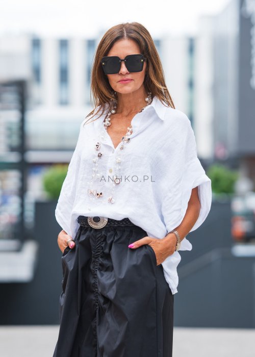 Biała, luźna koszula z kołnierzykiem, czarne spodnie z ozdobnym paskiem i długi naszyjnik z perełkami.