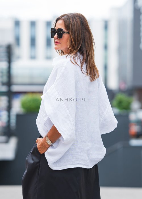 Biała, luźna koszula z kołnierzykiem, czarne spodnie z ozdobnym paskiem i długi naszyjnik z perełkami.