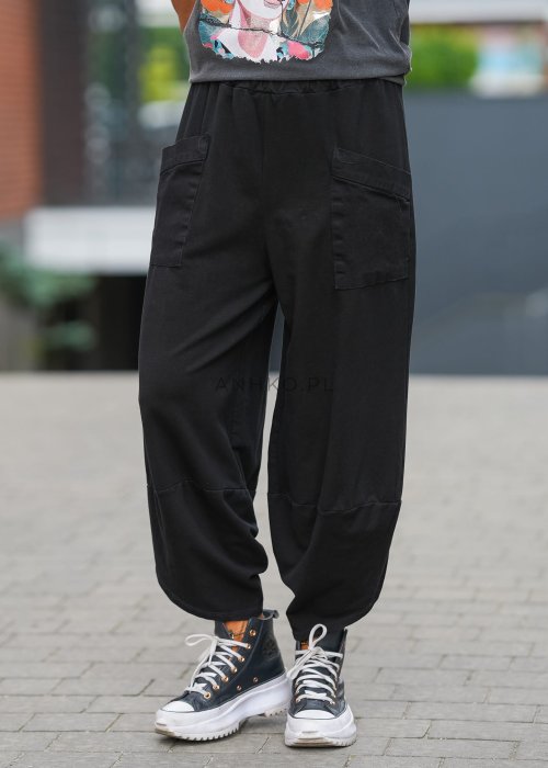 Czarne spodnie damskie o szerokim kroju typu bombka z dużymi kieszeniami i elastyczną talią. Stylizacja z t-shirtem i sneakersami w miejskim, casualowym wydaniu.