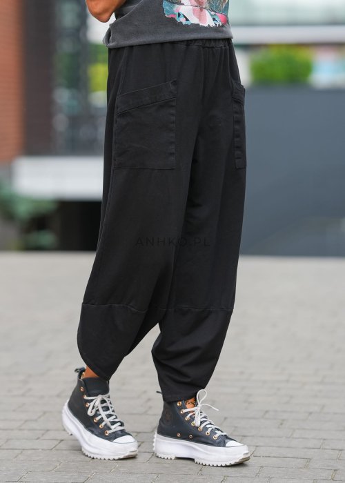 Czarne spodnie damskie o szerokim kroju typu bombka z dużymi kieszeniami i elastyczną talią. Stylizacja z t-shirtem i sneakersami w miejskim, casualowym wydaniu.