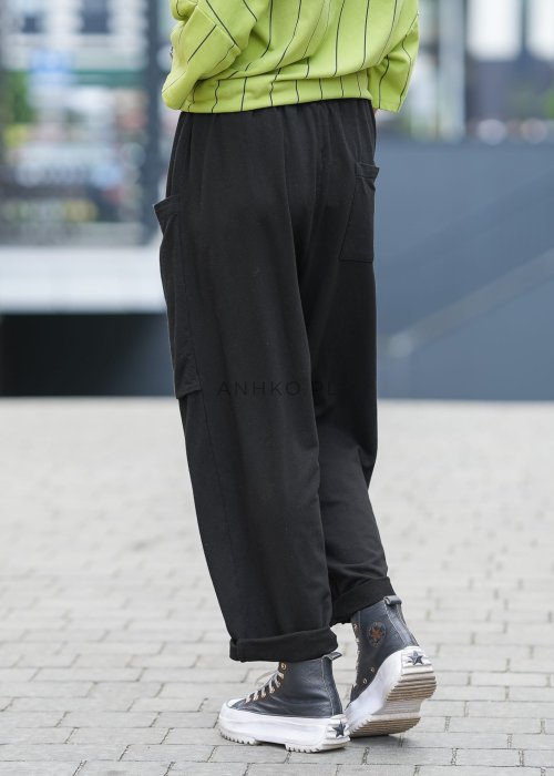 Czarne spodnie damskie o luźnym kroju z elastycznym pasem i dużymi naszywanymi kieszeniami z przodu. Model zestawiony ze sneakersami i zieloną bluzą w paski w miejskiej stylizacji