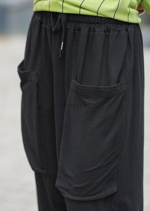 Czarne spodnie damskie o luźnym kroju z elastycznym pasem i dużymi naszywanymi kieszeniami z przodu. Model zestawiony ze sneakersami i zieloną bluzą w paski w miejskiej stylizacji